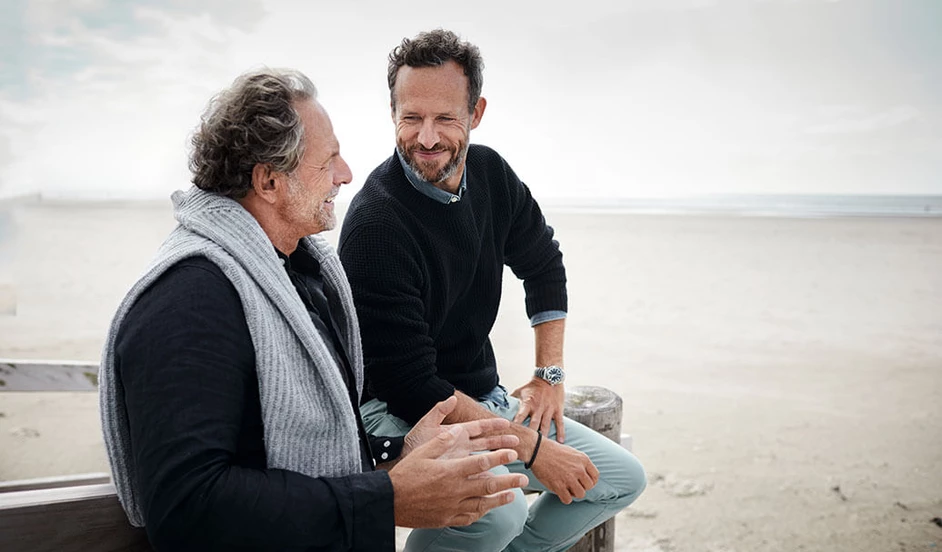 Zwei Männer sitzen am Strand und unterhalten sich.